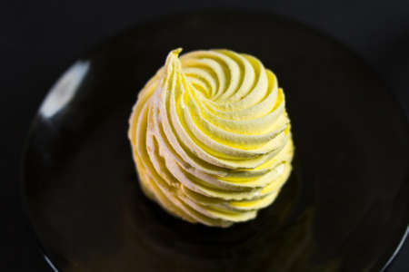 Yellow meringue on dark plate with black background. Food harmful to diabetics. Sweet addiction concept.の写真素材