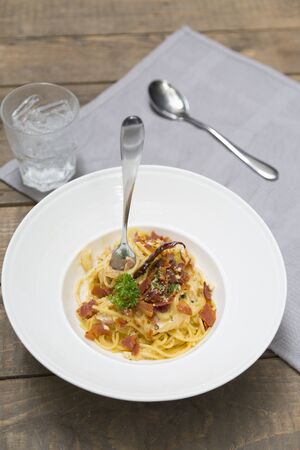 Dish of traditional spaghetti a la carbonara  with bacon  fork and spoon on table napkinの写真素材