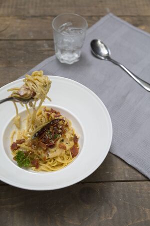 Dish of traditional spaghetti a la carbonara  with bacon  fork and spoon on table napkinの写真素材