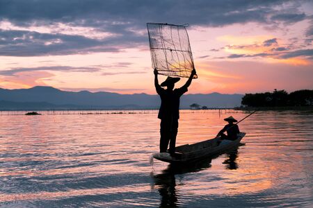 Silhouette of fisherman is traditional thai fishing style,  sunset time, at Kwan Phayao lake, Phayao province, Thailandの写真素材