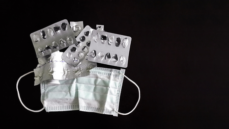 Medical face mask and used packs of pills isolated on black background. Surgical Ear-Loop Mask   with used empty Blister and Strip packs isolated. surgeon face mask.の写真素材