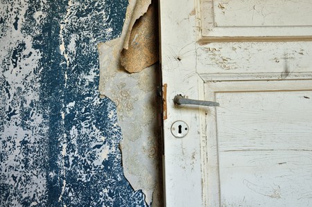 Torn vintage wallpaper peeling paint wall and wooden door in abandoned house.の写真素材