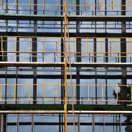 Facade windows and iron scaffold detail. Modern glass building under construction.の写真素材