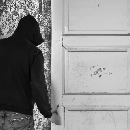 Hooded figure exiting through the door of an abandoned house.の写真素材