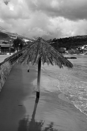 Sandy beach in the wintertime and parasol with palm tree leaves. Black and white.の写真素材