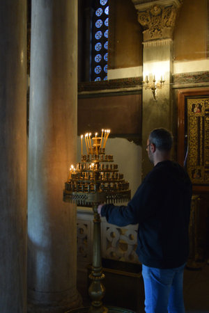 ATHENS GREECE  APRIL 27 2015: Man and antique manouali candle stand in byzantine church interior.のeditorial素材