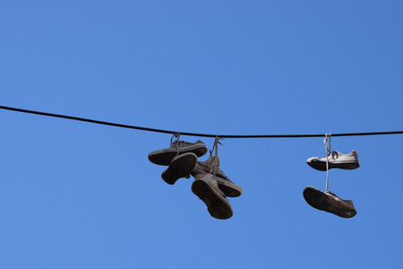 Shoe tossing old sneakers footwear with tied shoelaces hanging from a wire.