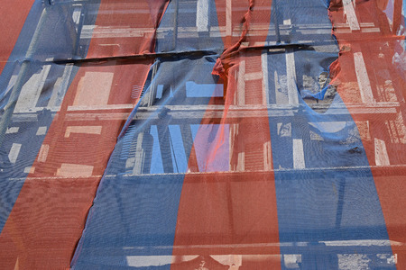 Abandoned building ready to fall down with scaffold support and covered by transparent colorful debris netting.の写真素材