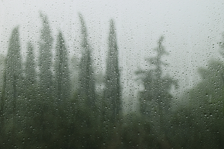Raindrops on window glass and distant forest trees. Rainy day abstract.の写真素材