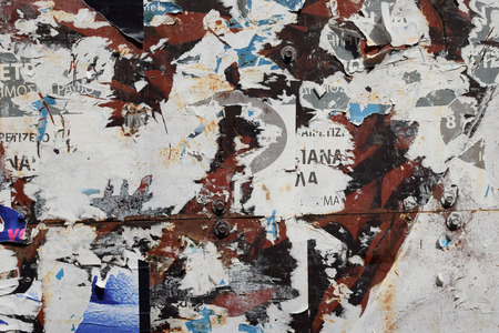 Rusty metal surface covered with torn posters. Abstract background texture.