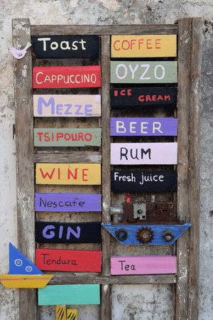 ZAKYNTHOS, GREECE - AUGUST 14, 2018: Wooden cafe bar drinks menu board sign with handmade decorative boats.のeditorial素材