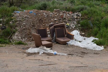 Old armchairs broken furniture and pile of debris rubble and trash by the side of the road. Illegal waste dumping spot.の写真素材