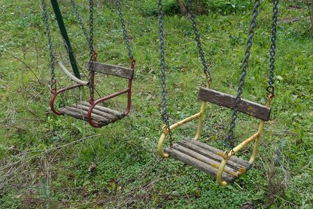 Vintage wooden swing seats in disused playground.