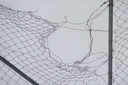 Damaged chain link fence abstract wire shapes and white snow background.