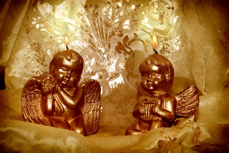 two candlelight Christmas angels with golden fabric backgroundの写真素材
