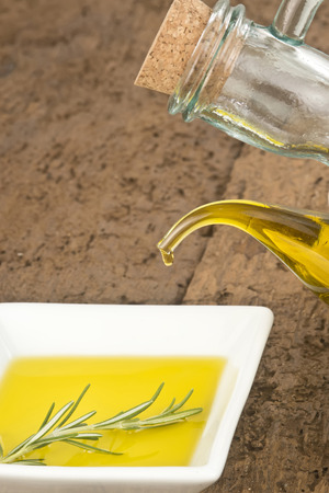 Bottle pouring virgin olive oil in a porcelain plate with rosemary on old wooden tableの写真素材