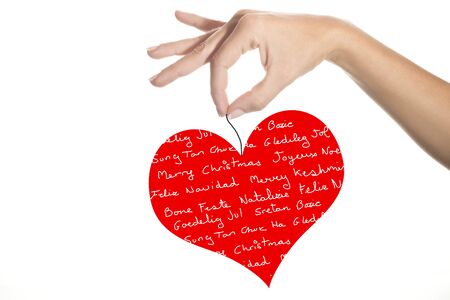 Christmas greeting card, girl hand holding a heart with the message Merry Christmas handwritten in different languagesの写真素材