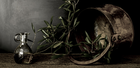 Olive oil and old copper pot and olive leaves on dark backgroundの写真素材