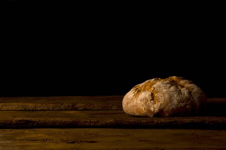 Still life of freshly baked bread with crust lying on wooden table on black background.の写真素材