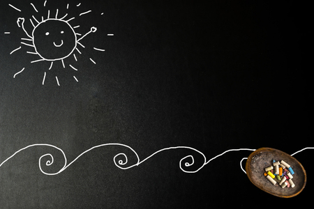 Happy sunny sun and beach card, chalk child drawing on a blackboard with copy space to write message.の写真素材