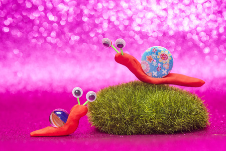 Fun children's background, two cute snails made with plasticine, marble and a button on pink background with space for text or photoの写真素材