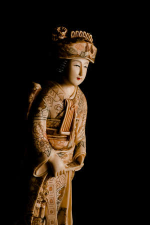 Old figure of a Japanese geisha in ivory decorated by hand on a black background, vertical image.の写真素材