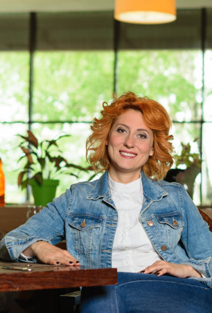 Beautiful, red-haired woman sitting in a chair in a restaurantの写真素材