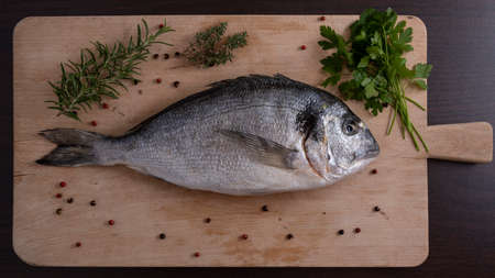 Raw sea bream on a wooden plank with pepper and herbs