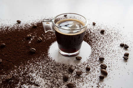 A cup of coffee with coffee beans and ground coffee around it