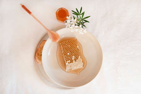 Honey and honeycomb on a white table with white flowersの写真素材