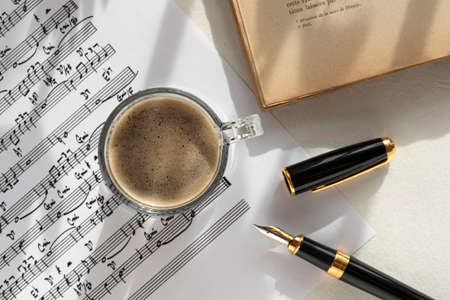 Black coffee cup on a music score, pen and bookの写真素材