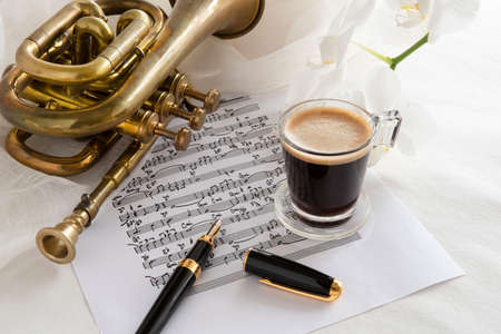 Black coffee cup on a music score with trumpet and flowerの写真素材