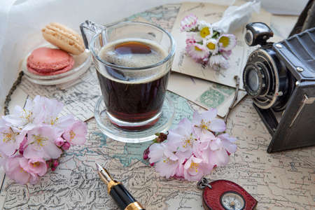 Black coffee in a cup, next to a world map and an old camera with spring flowers on the tableの写真素材