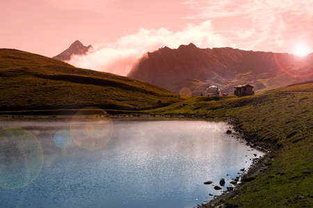 High altitude mountain landscape with the mountain reflected in a lake and a sunsetの写真素材
