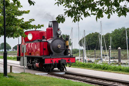 Old red steam train by the sea with boats in Picardie, Franceの写真素材