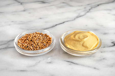 Close-up of mustard seeds and yellow mustard in glass bowlsの写真素材