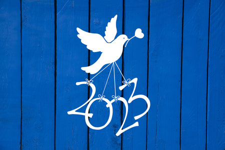 A dove carries the numbers of the new year 2023 on a blue wooden backgroundの写真素材