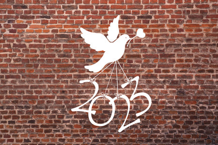 A dove carries the numbers of the new year 2023 on a red brick backgroundの写真素材