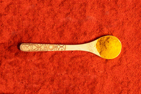 Close-up of a wooden spoon with turmeric on a red paprika textureの写真素材