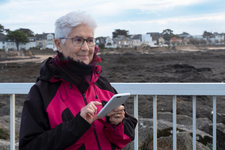 A senior Caucasian woman writes a message on her mobile phone outside in Brittanyの写真素材