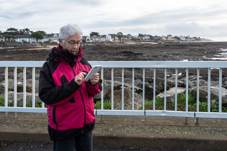 A senior Caucasian woman writes a message on her mobile phone outside in Brittanyの写真素材