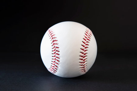 Close-up of a white baseball with red stitching on a black backgroundの写真素材