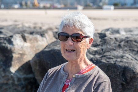A senior woman on a beach in summer with white hair and sunglassesの写真素材