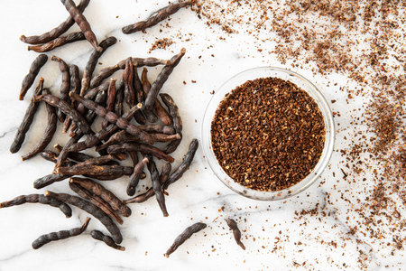 Close-up of elongated African black pepper pods on a white marble background, with ground pepper next to themの写真素材