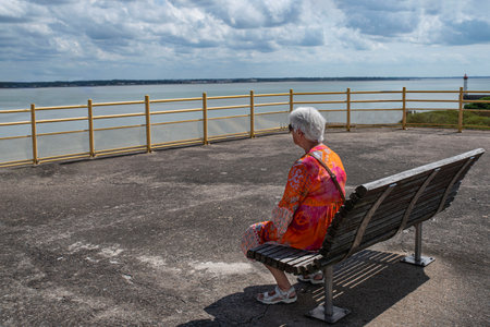 An elderly woman sitting on a bench looking out to seaの写真素材