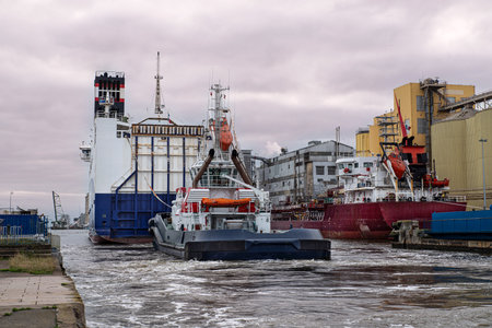 Large Ro-Ro (roll on-roll off) cargo ship in the port of Saint-Nazaire in Brittany, France, with warehouses and an agricultural silo for grain storageの写真素材