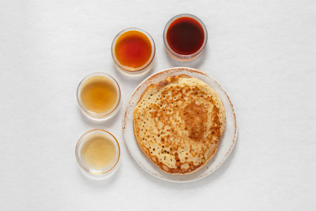 Different classes of maple syrups in different colors in glass bowls with pancakes next to themの写真素材