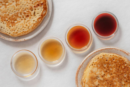 Different classes of maple syrups in different colors in glass bowls with pancakes next to themの写真素材