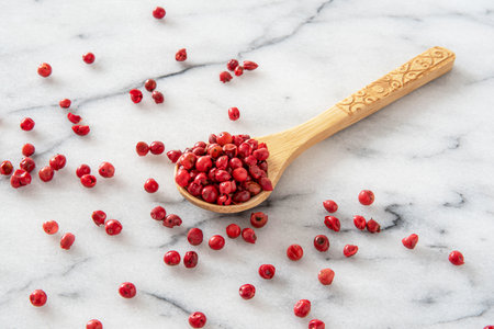 Red peppercorns in wooden spoon on white marble table background.の写真素材