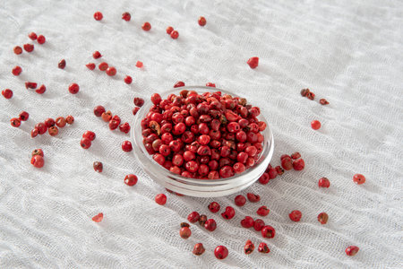 Red peppercorns in a glass bowl on a white tableclothの写真素材